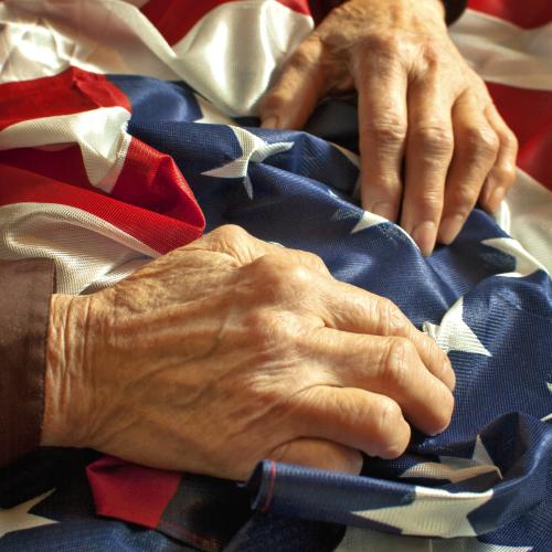 Man's wrinkled hands rest on the American Flag
