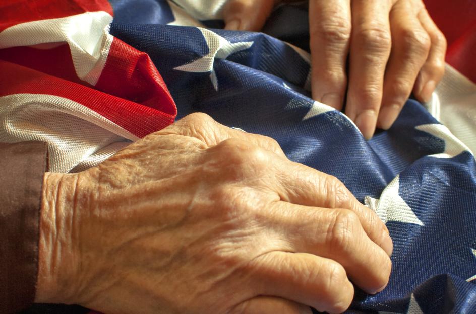 Man's wrinkled hands rest on the American Flag