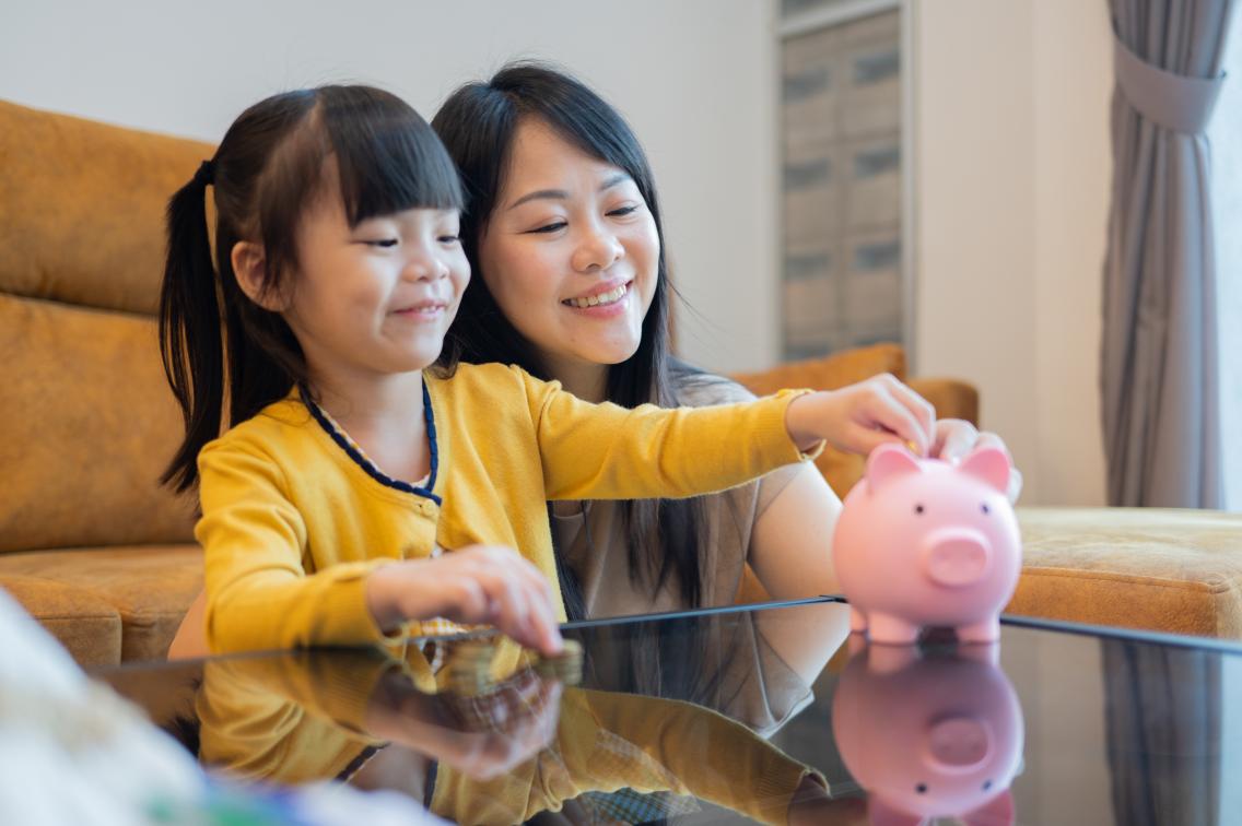 mother and daughter putting money into piggy bank